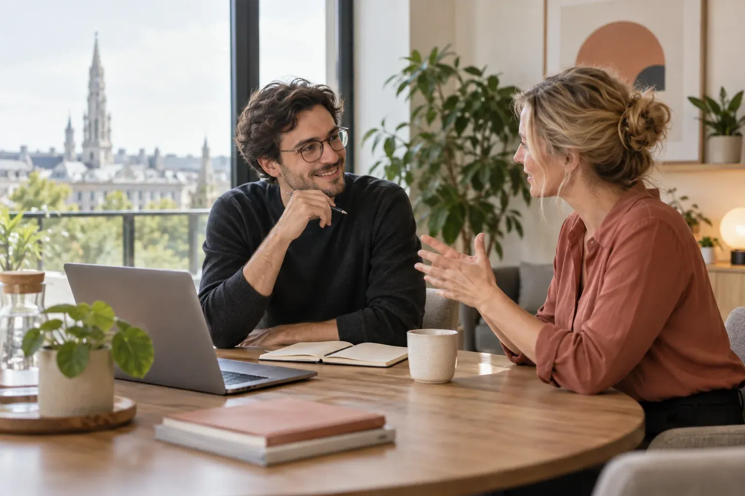 Premier contact : un conseiller échange avec une cliente autour d'un ordinateur portable, avec vue sur Bruxelles